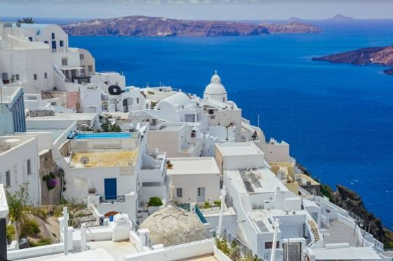 Santorini panoramic view featuring iconic whitewashed cliffside villages, blue-domed churches, luxury hotels, volcanic caldera, crystal-clear Aegean Sea, breathtaking sunset scenery, private yacht charters, helicopter transfers, and exclusive VIP travel experiences in Greece.